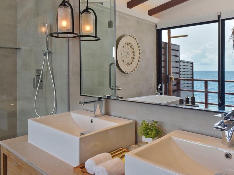 Salle de bain d'hôtel moderne avec deux lavabos et vue sur la mer par une grande fenêtre.