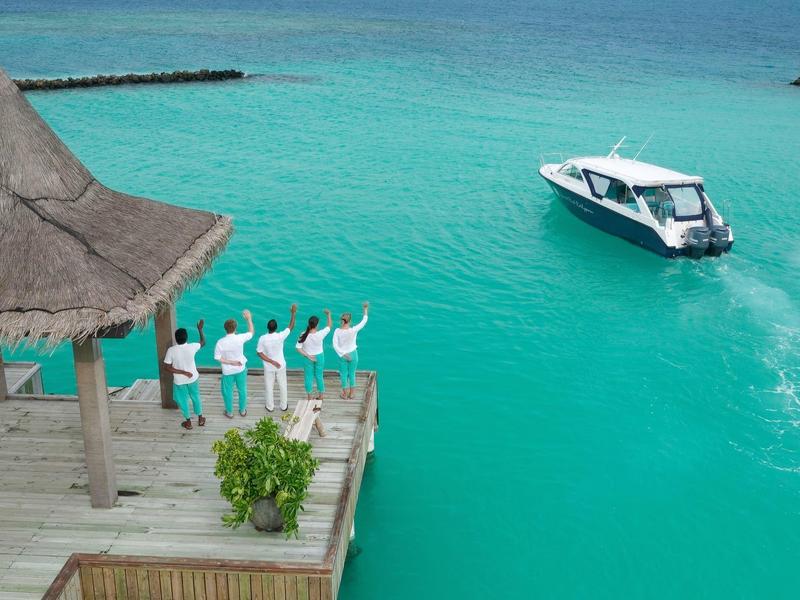 Des gens saluent un bateau depuis une jetée dans une eau turquoise