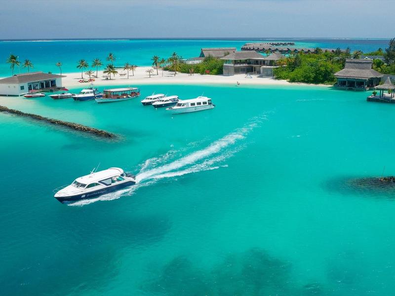Vue sur une île avec complexe hôtelier et bateau dans une eau turquoise claire