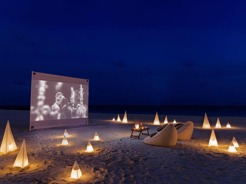 Cinéma en plein air nocturne sur la plage avec des lanternes lumineuses et des chaises sur le sable