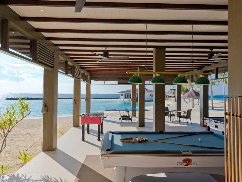 Espace de jeux couvert avec billard, baby-foot et vue sur la plage et la mer.
