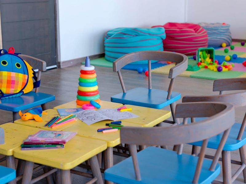 Espace de jeu coloré pour enfants avec tables, chaises et divers jouets dans une pièce lumineuse.
