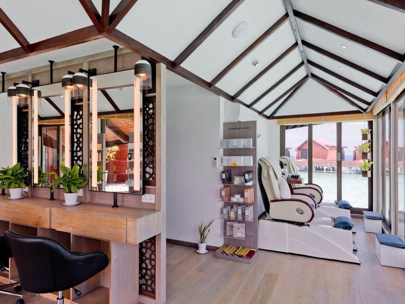 Espace bien-être moderne avec fauteuils de massage et coin salon confortable près de grandes fenêtres.