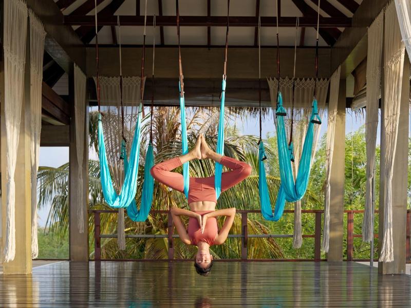 Personne faisant du yoga dans un pavillon ouvert avec des hamacs bleus et un environnement tropical.