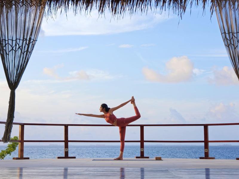 Personne pratique une posture de yoga sur une terrasse avec vue sur la mer et ciel bleu.