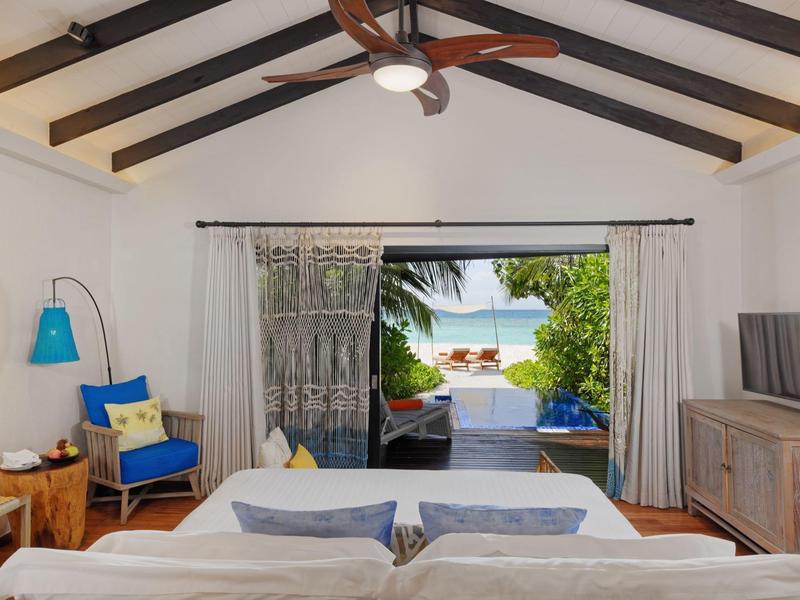 Chambre d'hôtel lumineuse avec lit double, coin salon et vue sur jardin tropical et mer.