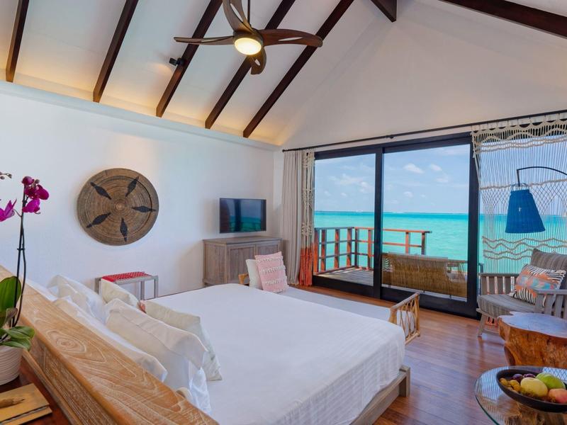 Chambre lumineuse avec plafond à poutres en bois, vue sur la mer et accès à un balcon.