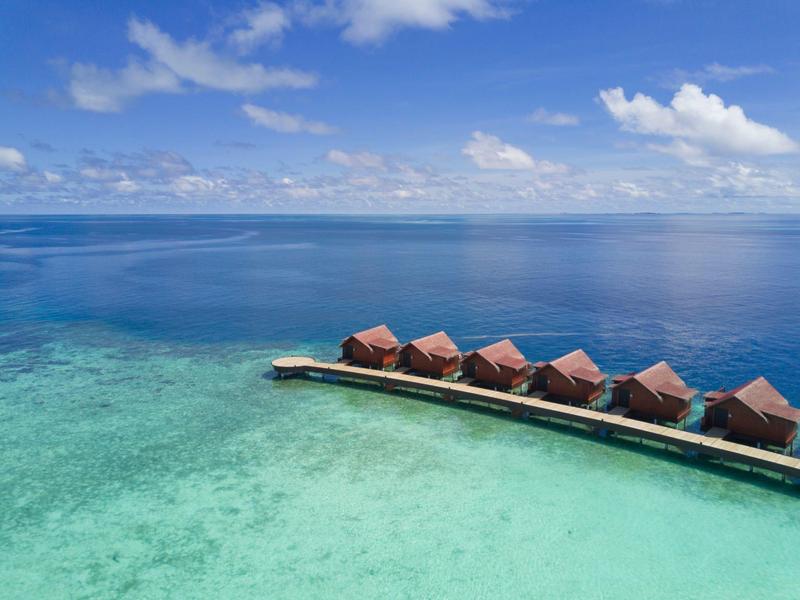 Bungalows sur pilotis au-dessus d'eau turquoise claire avec ciel bleu et nuages.