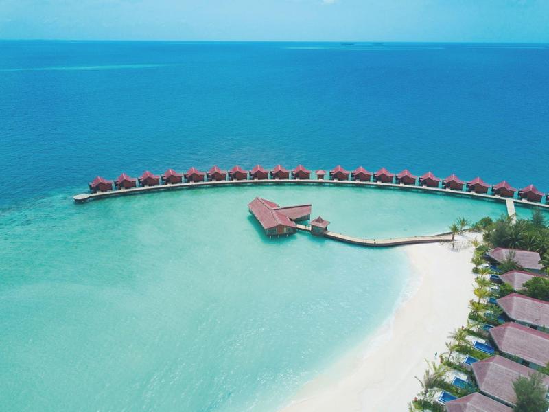 Bungalows de luxe sur l'eau au-dessus d'une eau turquoise près d'une plage de sable blanc.