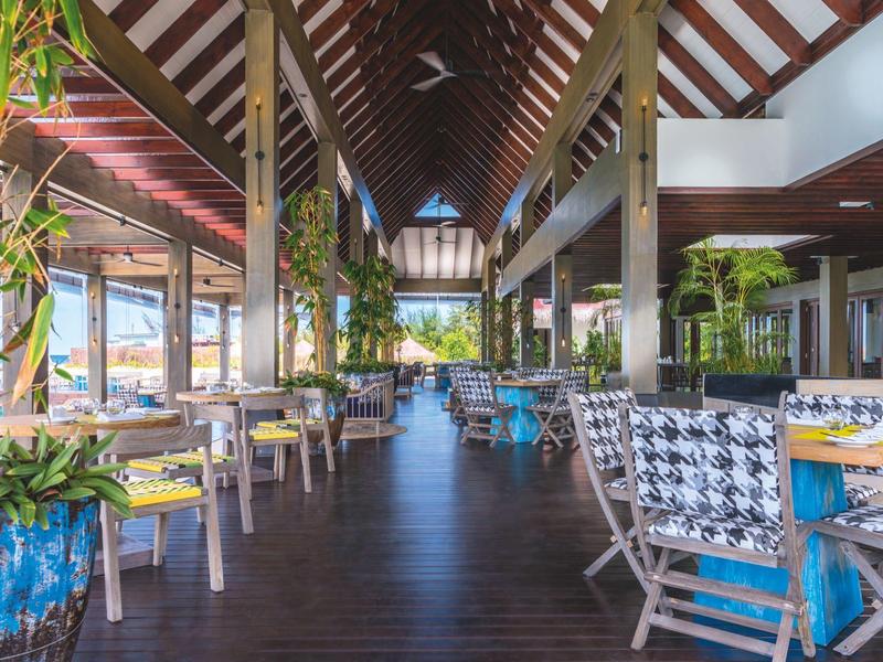 Restaurant lumineux avec mobilier en bois, de nombreuses plantes et vue sur l'eau.