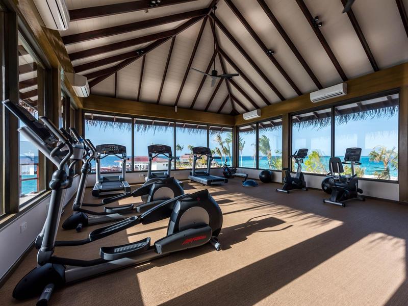 Salle de sport avec appareils cardio et vue sur l'océan à travers de grandes fenêtres.