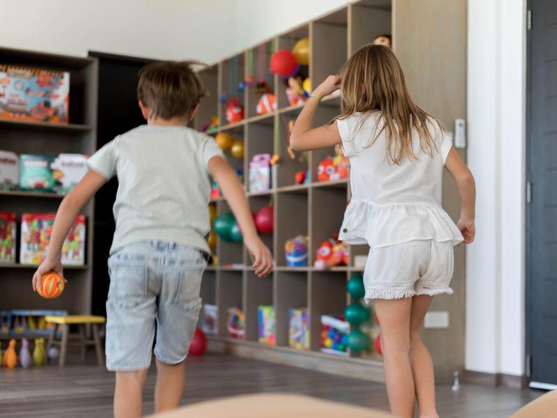 Des enfants jouent avec des balles colorées dans une salle de jeu lumineuse avec des étagères.