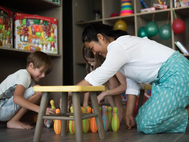 Une femme et deux enfants jouent avec des quilles colorées sur le sol dans une pièce.