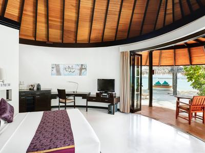 Habitación de hotel luminosa con techo de madera, escritorio, cama grande y terraza con vista al mar.