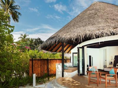 Bungalow con techo de paja y terraza abierta en entorno tropical bajo cielo azul.