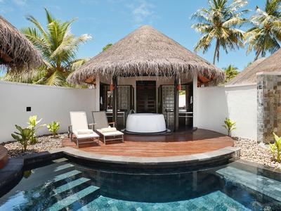 Piscina privada frente a bungalow con techo de paja y tumbonas, rodeado de palmeras.