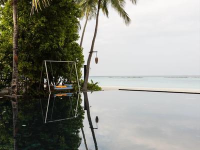 Ein Infinity-Pool mit Palmen und ruhigem Wasser, das den Himmel und die Palmen spiegelt.