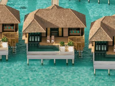 Überwasser-Bungalows mit Strohgedeck über klarem, türkisfarbenem Wasser.