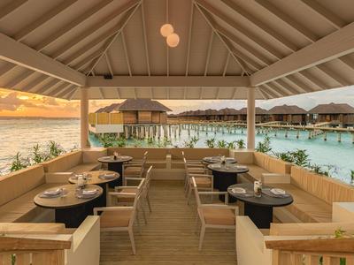 Offene Restaurantterrasse mit Blick auf das Wasser und Sonnenuntergang unter einem hohen Holzdach.