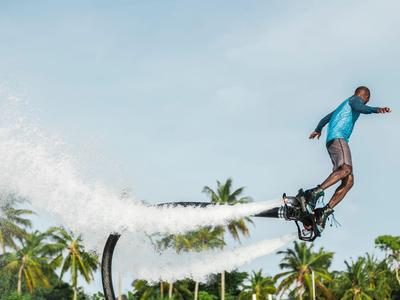 Mann mit Flyboard über Wasser mit Palmen im Hintergrund