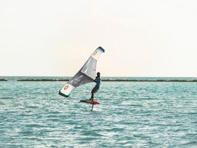 Person steht auf einem Hydrofoil-Surfbrett mit Segel auf offenem Wasser.