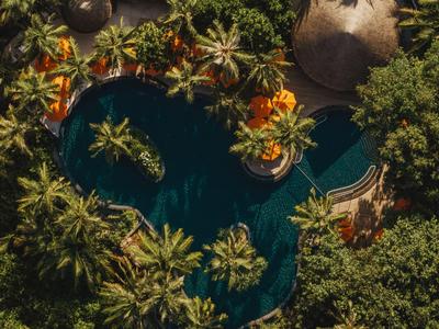Vogelperspektive auf eine tropische Hotelpoollandschaft mit Palmen und Sonnenschirmen