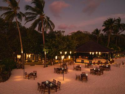 Strandrestaurant mit Tischen und Stühlen bei Sonnenuntergang, umgeben von Palmen.