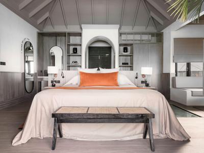 Modernes Hotelzimmer mit großem Bett, orangefarbener Kissen, Holzboden und stimmungsvoller Beleuchtung.