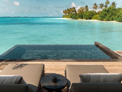 Zwei bequeme Liegen an einem Infinity-Pool mit Blick auf das türkisfarbene Meer und eine Insel.