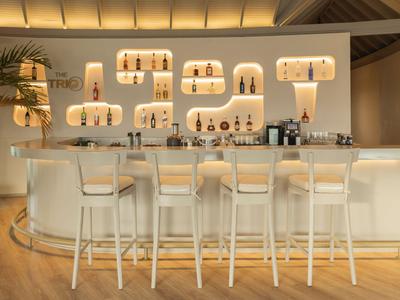 Moderner Hotelbarbereich mit weißen Barhockern und stilvoll illuminierten Regalen an der Wand.