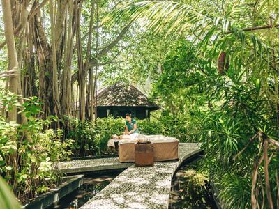 Weg aus Steinplatten führt durch üppigen tropischen Garten zu einem kleinen Gebäude.