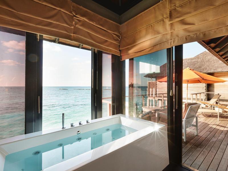 Jacuzzi moderno en una suite con vistas al mar y terraza de madera con tumbonas.