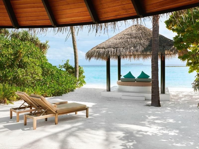 Playa con tumbonas y palmeras, vista al mar bajo un techo de paja