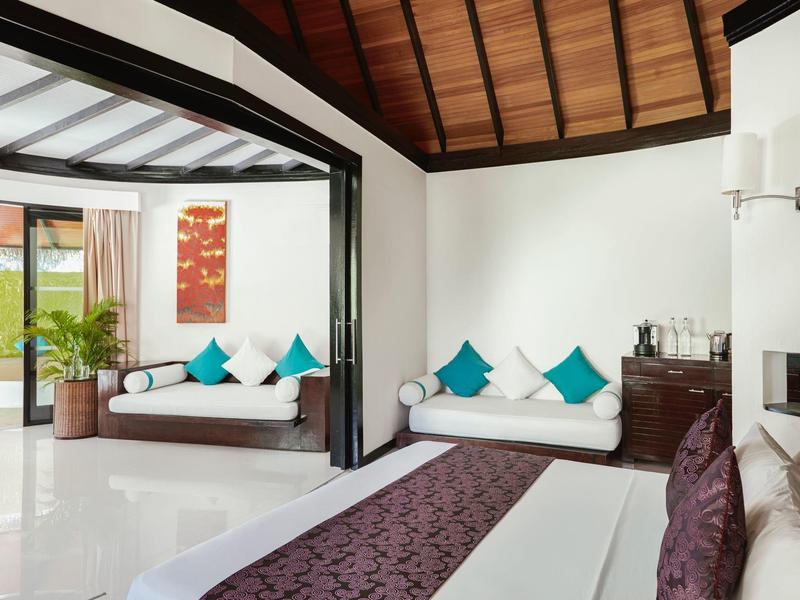 Habitación de hotel moderna con paredes blancas, techo de madera y cómodos sofás con cojines coloridos.