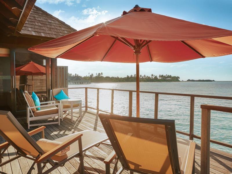 Balcón con sillas y sombrilla con vistas al agua bajo cielo despejado.