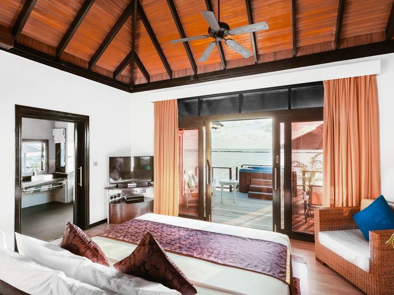 Habitación de hotel luminosa con techo de madera, cama doble, TV y acceso a terraza con vista al mar.