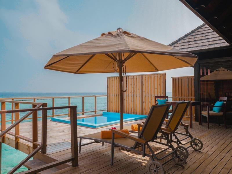 Terraza de madera con piscina, dos tumbonas y gran sombrilla con vistas al mar.