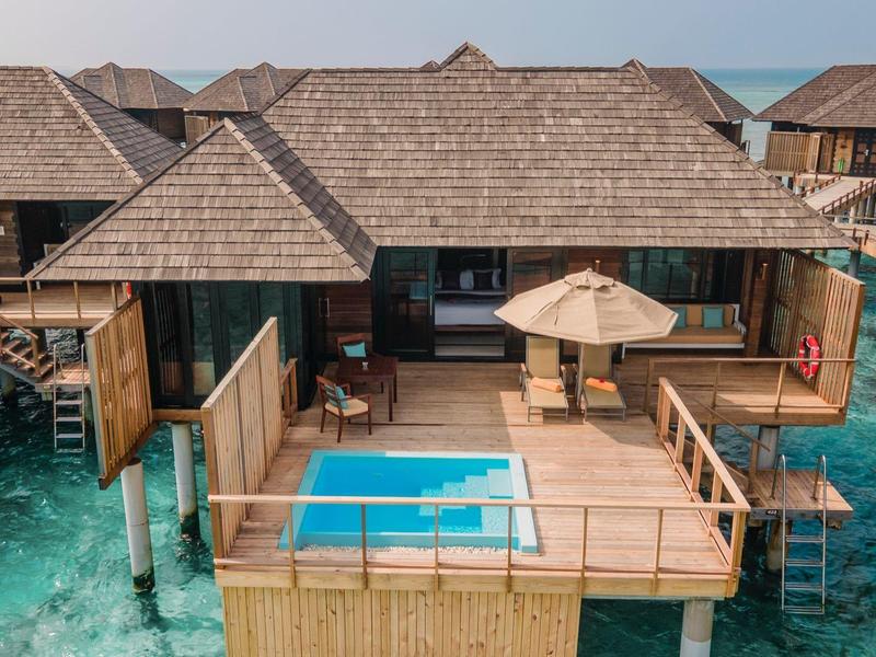 Villa de lujo sobre el agua con piscina y terraza de madera sobre agua azul clara.