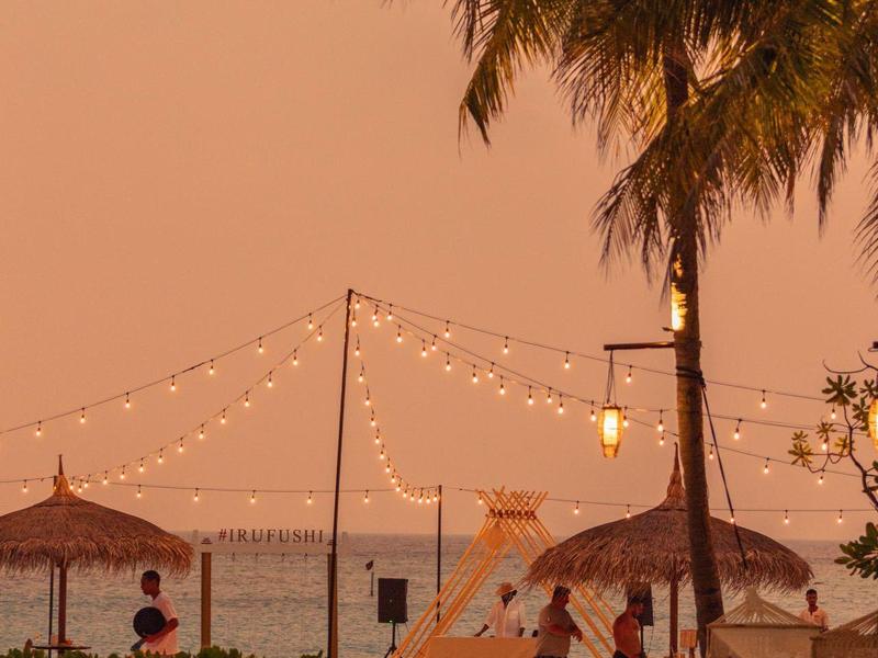 Palmeras y playa con luces y personas al atardecer junto a la piscina del hotel.
