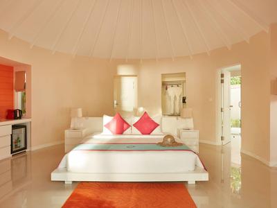 Helles Schlafzimmer mit weißem Bett, roten Kissen und orangem Teppich in modernem Stil.