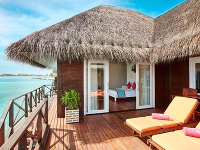 Bungalow mit Strohdach und Liegestühlen auf hölzerner Terrasse am Meer.