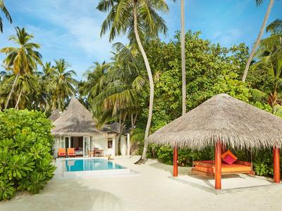Tropisches Resort mit Pool, Strandbett und Palmen unter blauem Himmel.
