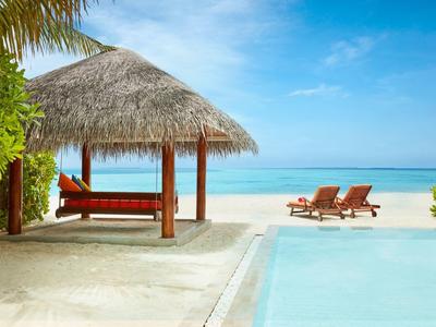 Strand mit Palmen, Pool und Liegestühlen unter blauem Himmel.