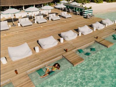 Strandresort mit Liegen auf Holzsteg über klarem Wasser und Palmen im Hintergrund.
