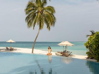 Infinity-Pool mit Blick auf weißen Sandstrand, Palmen und türkisfarbenes Meer.