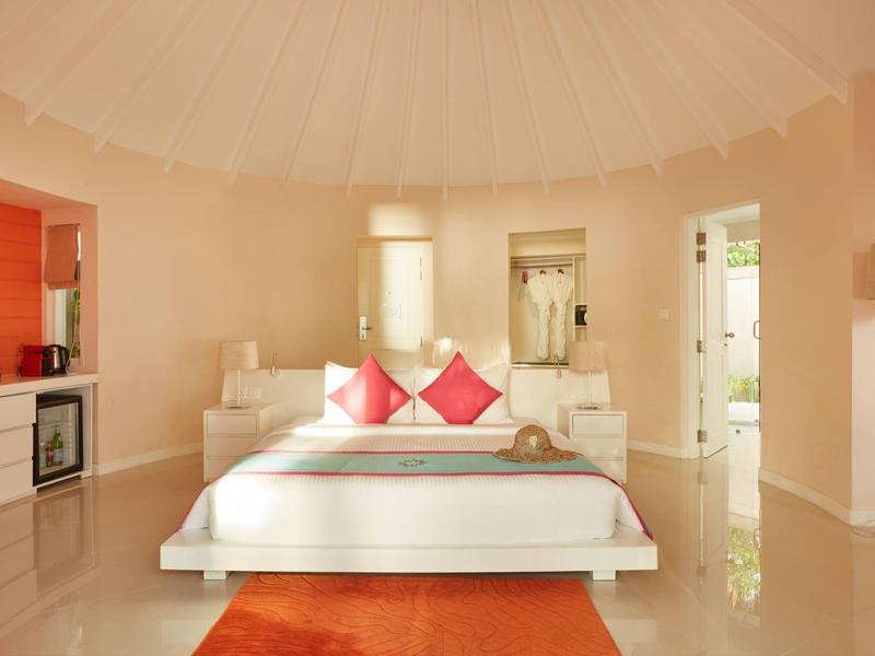 Camera luminosa con letto bianco, cuscini rossi e tappeto arancione in stile moderno.