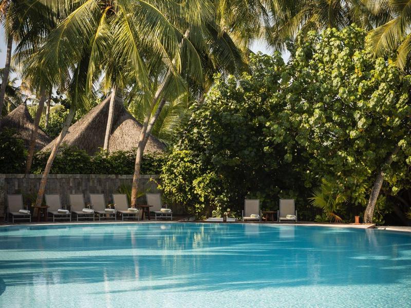 Una piscina d'hotel limpida con palme e lettini sullo sfondo.