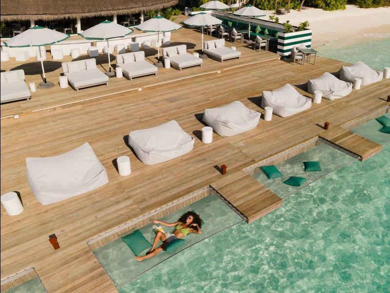 Resort sulla spiaggia con lettini su molo di legno sull'acqua limpida e palme.