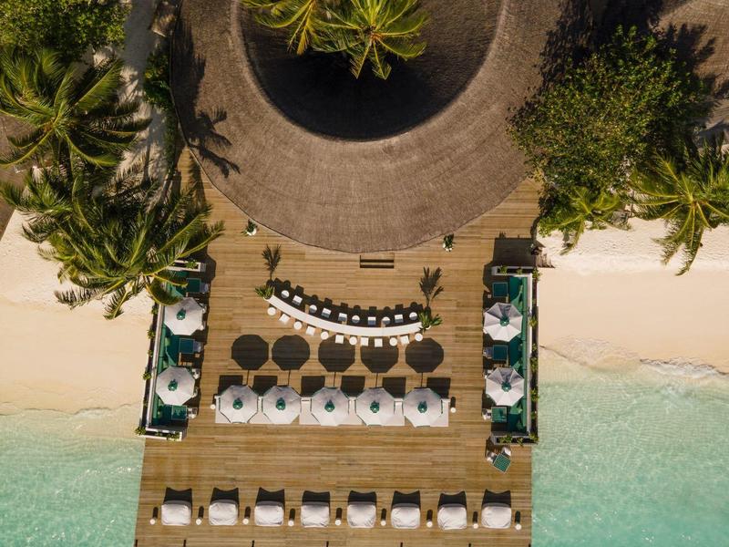 Vista aerea di una passerella in legno con lettini e ombrelloni sulla spiaggia accanto all'acqua turchese.