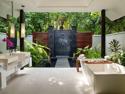 Otwarta łazienka z wolnostojącą wanną i prysznicem na zewnątrz w tropikalnym otoczeniu.